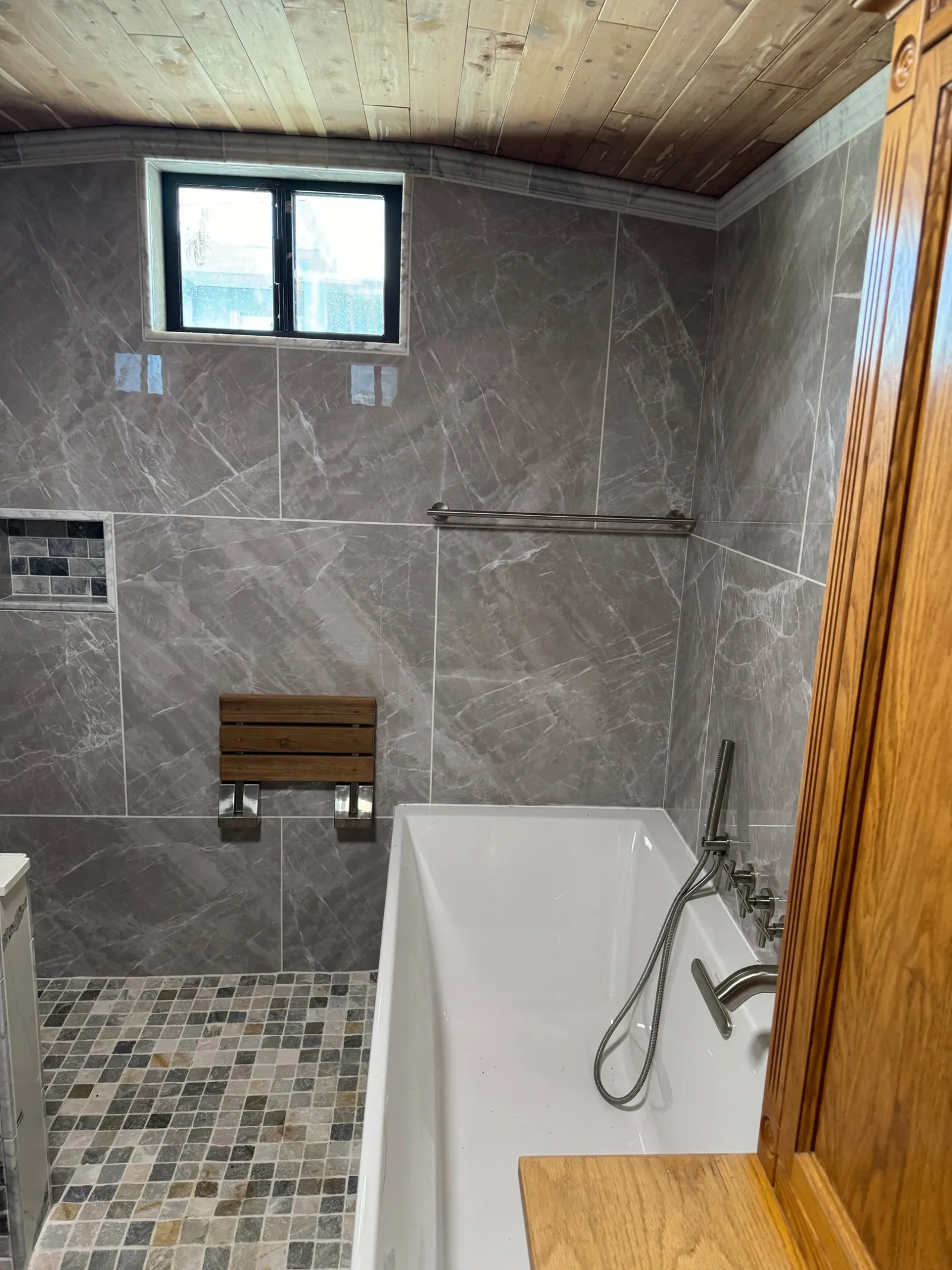 Grey marble-look tile, a wood plank ceiling and a teak shower seat.