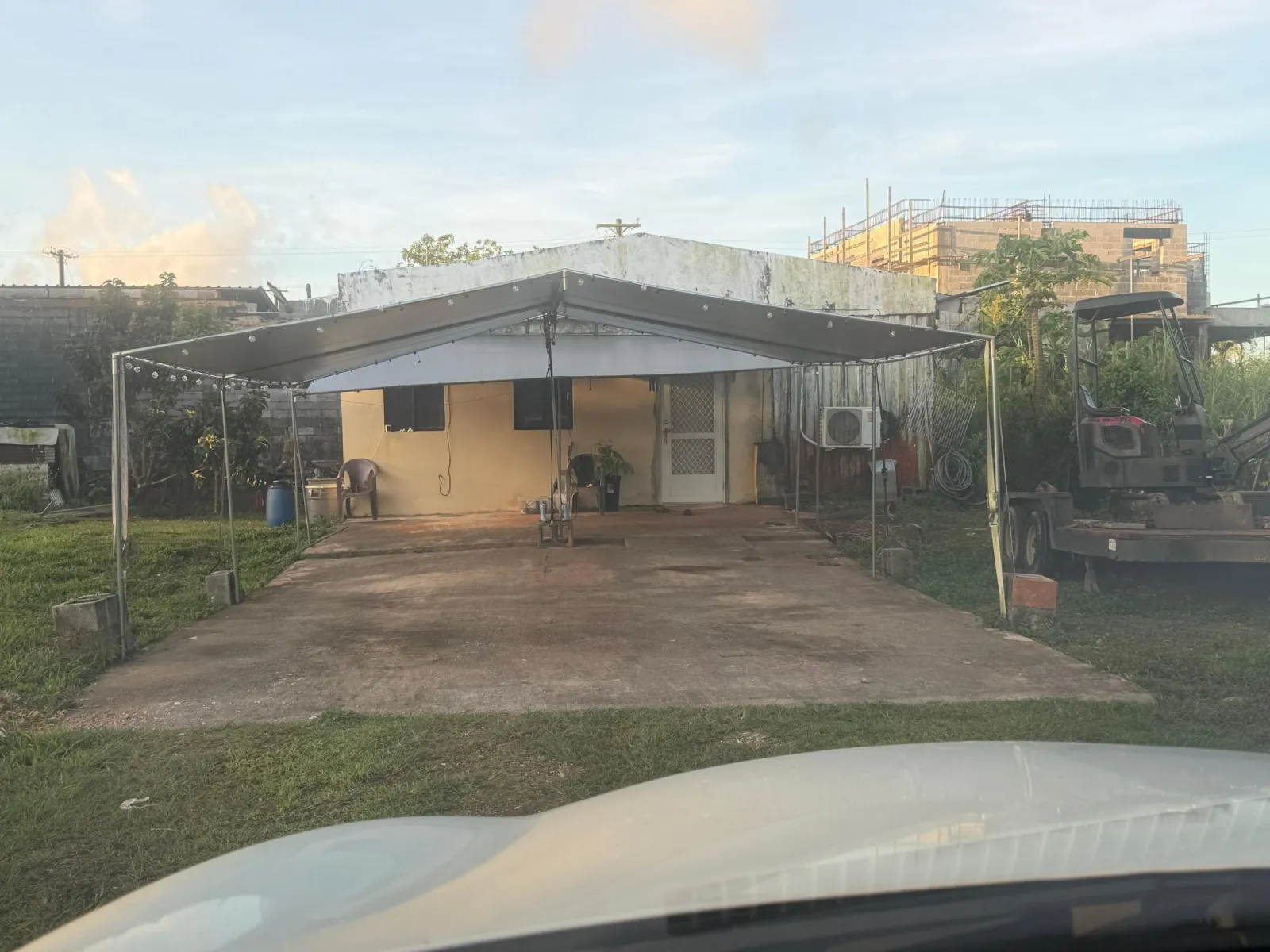 A sagging tarp canopy on thin steel poles over a stained concrete pad