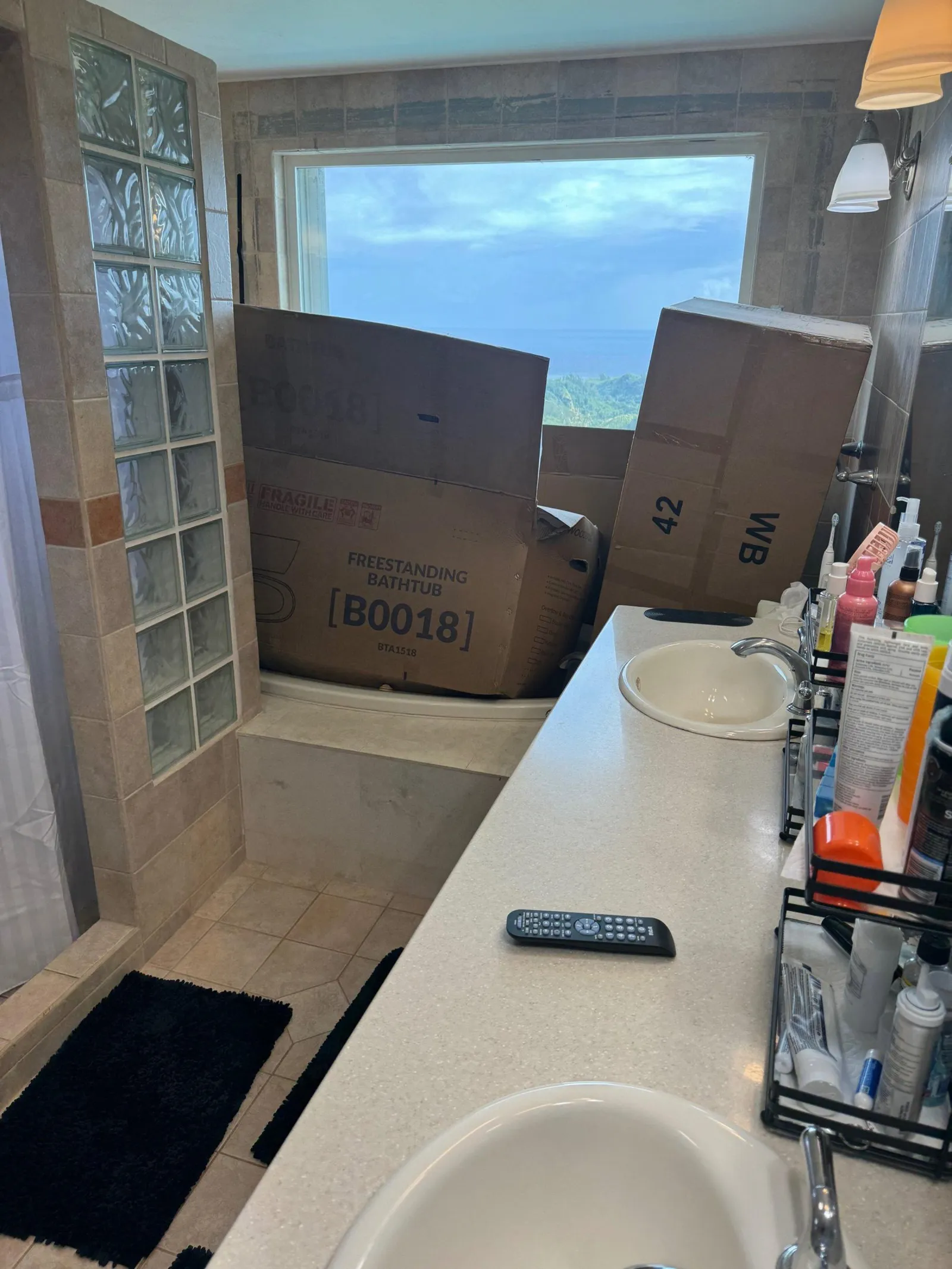Dated bathroom with beige tile, a glass block wall and a drop-in tub, the new fixtures still boxed